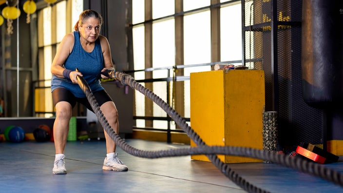 A woman trains with battle ropes at the gym.