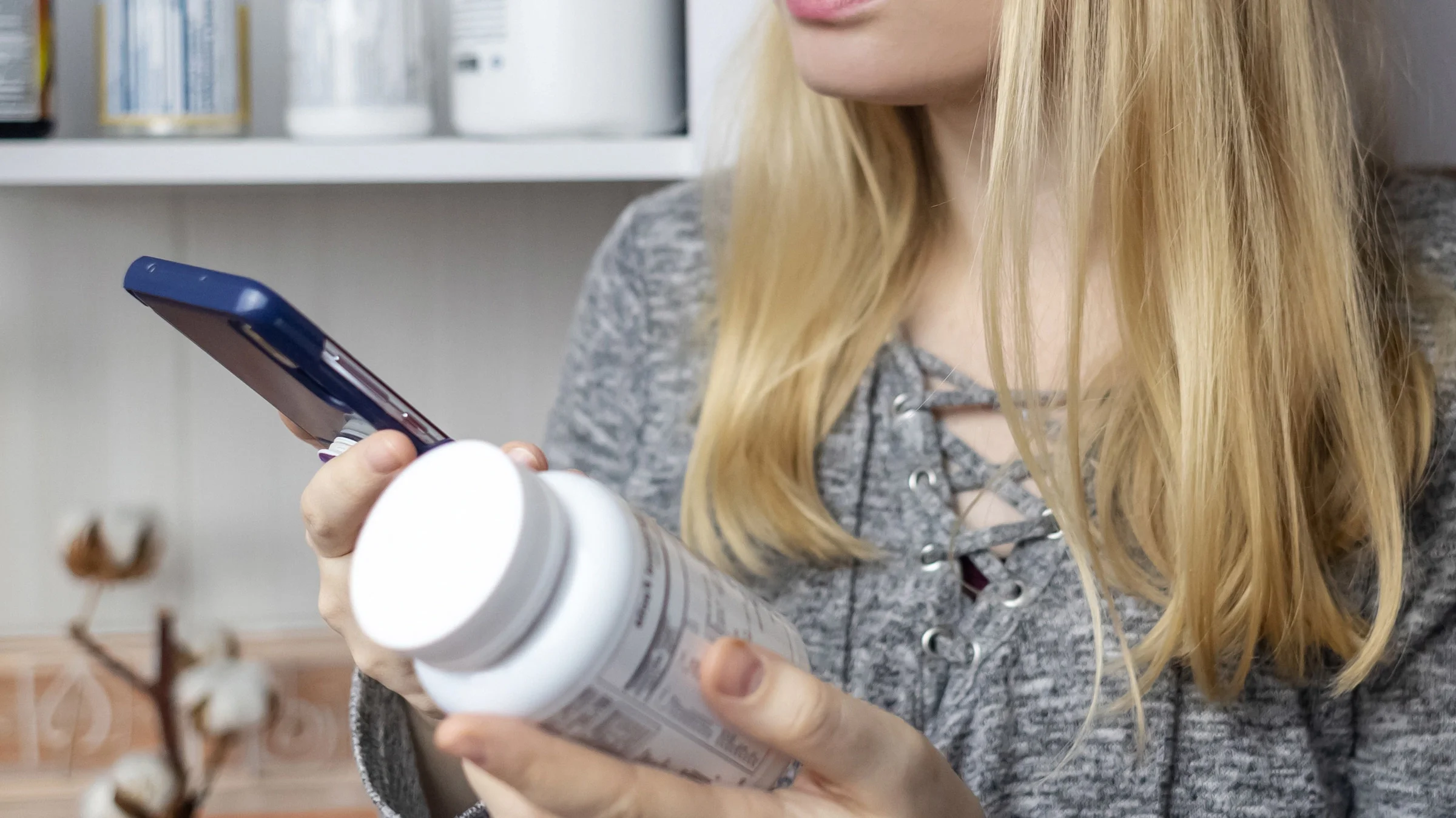 Closeup of someone holding a supplement bottle and looking it up on their phone.