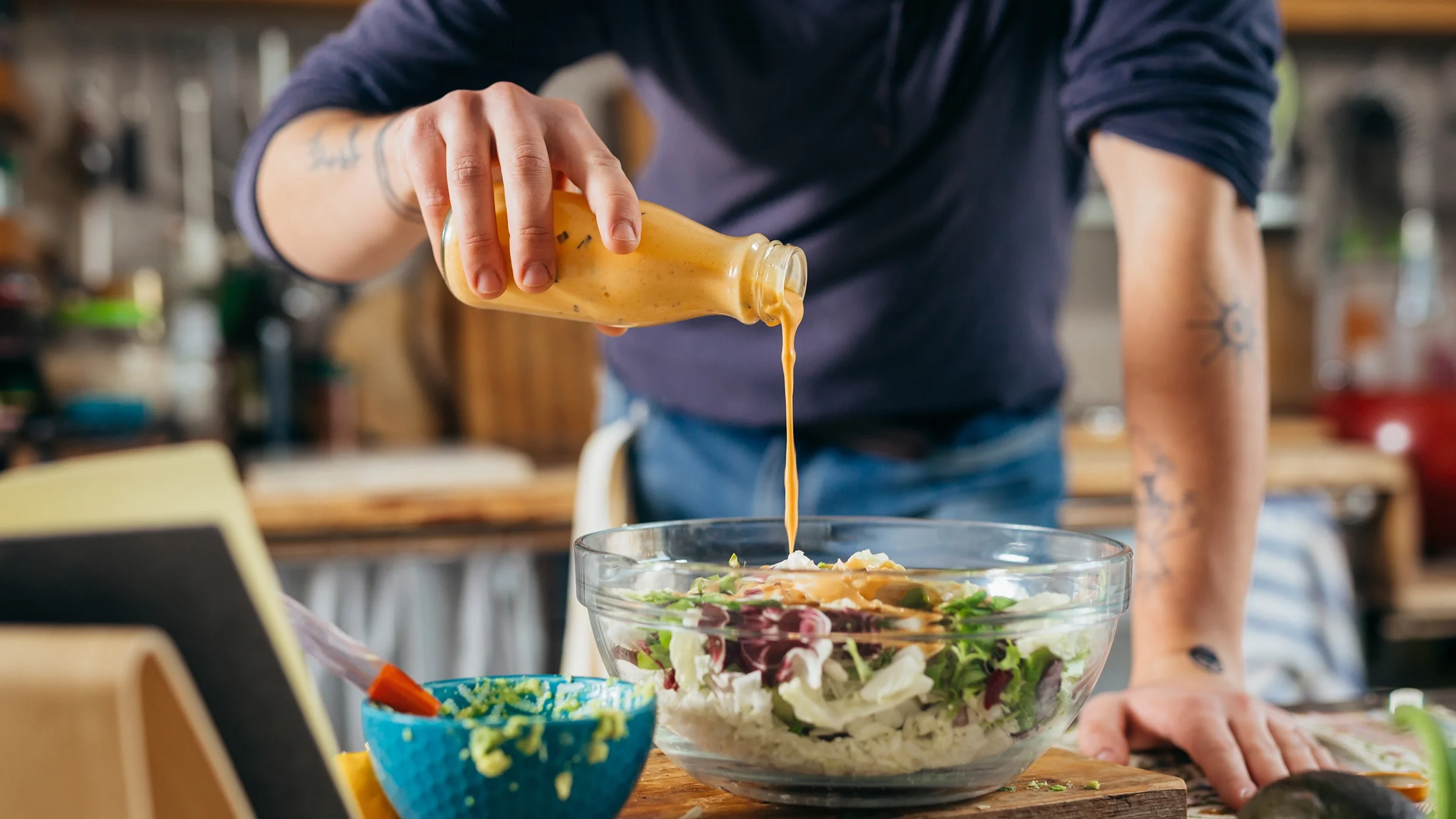 A man pours dressing on a salad. 