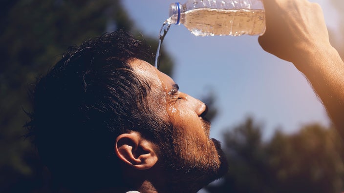 Close-up of a man pouring water on his face on a hot day.