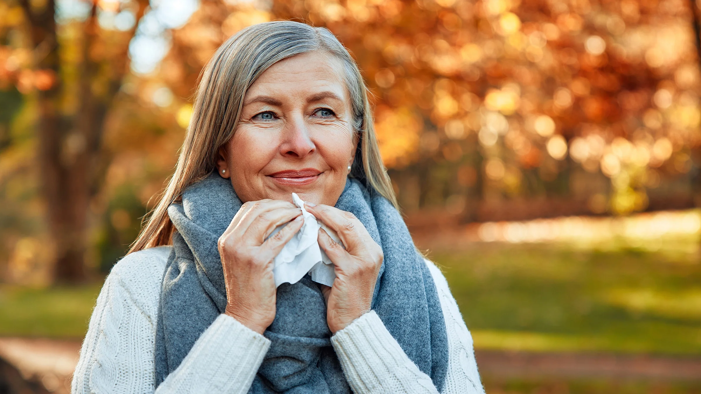 A woman stands outside and holds a tissue for blowing her nose.