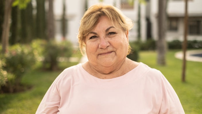 Portrait of a woman with a soft smile and expression on her face. She is outside in a park.