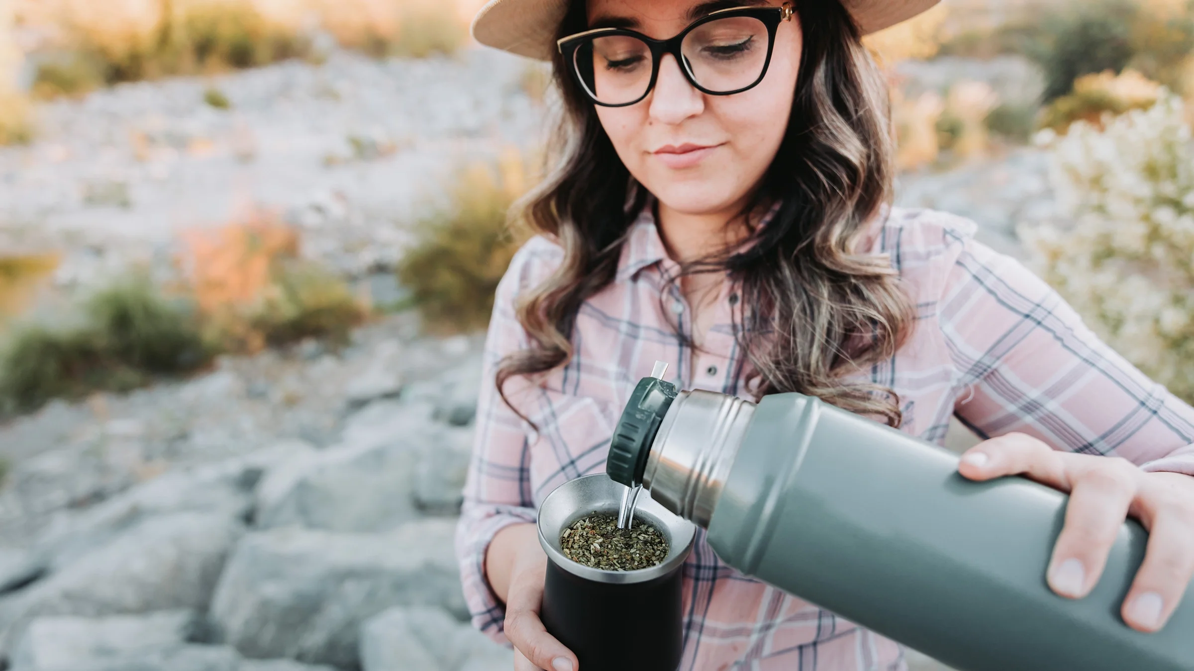 Woman pouring yerba mate in a green thermos.