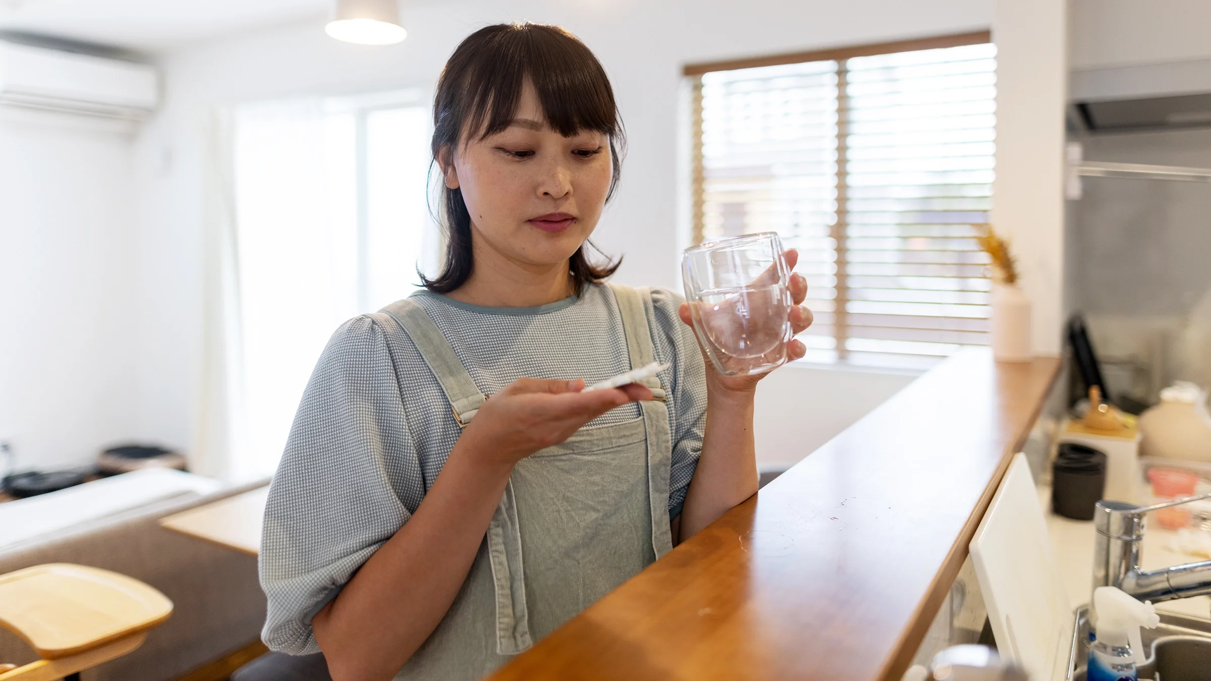 A woman prepares to take a pill with a glass of water.