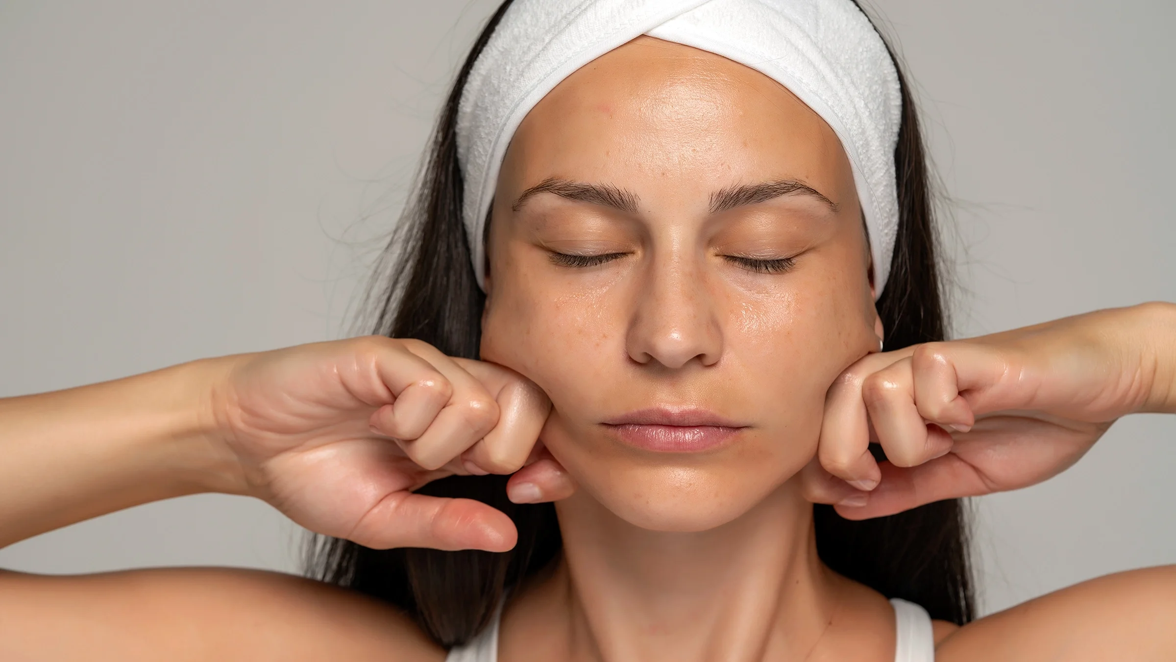 Woman massaging her face on a gray background.