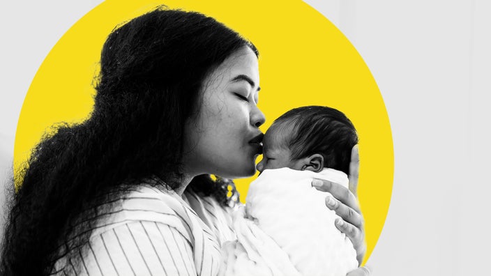 Black and white photo of a mother kissing her newborn on the forehead. There is an added yellow graphic circled behind her and the baby.