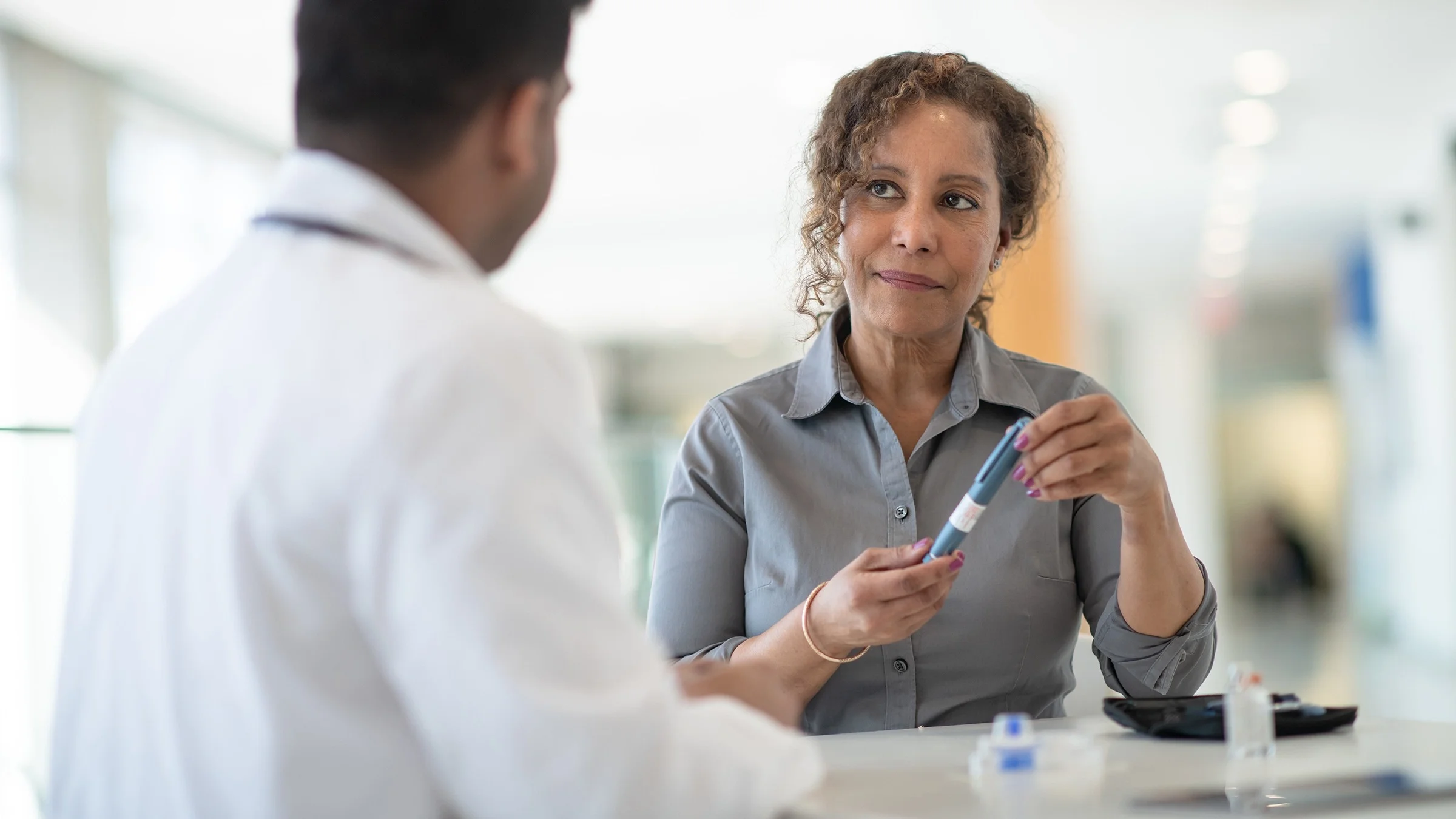 Middle age woman speaking to her doctor for an insulin consultation. She is holding an insulin pen in her hands.