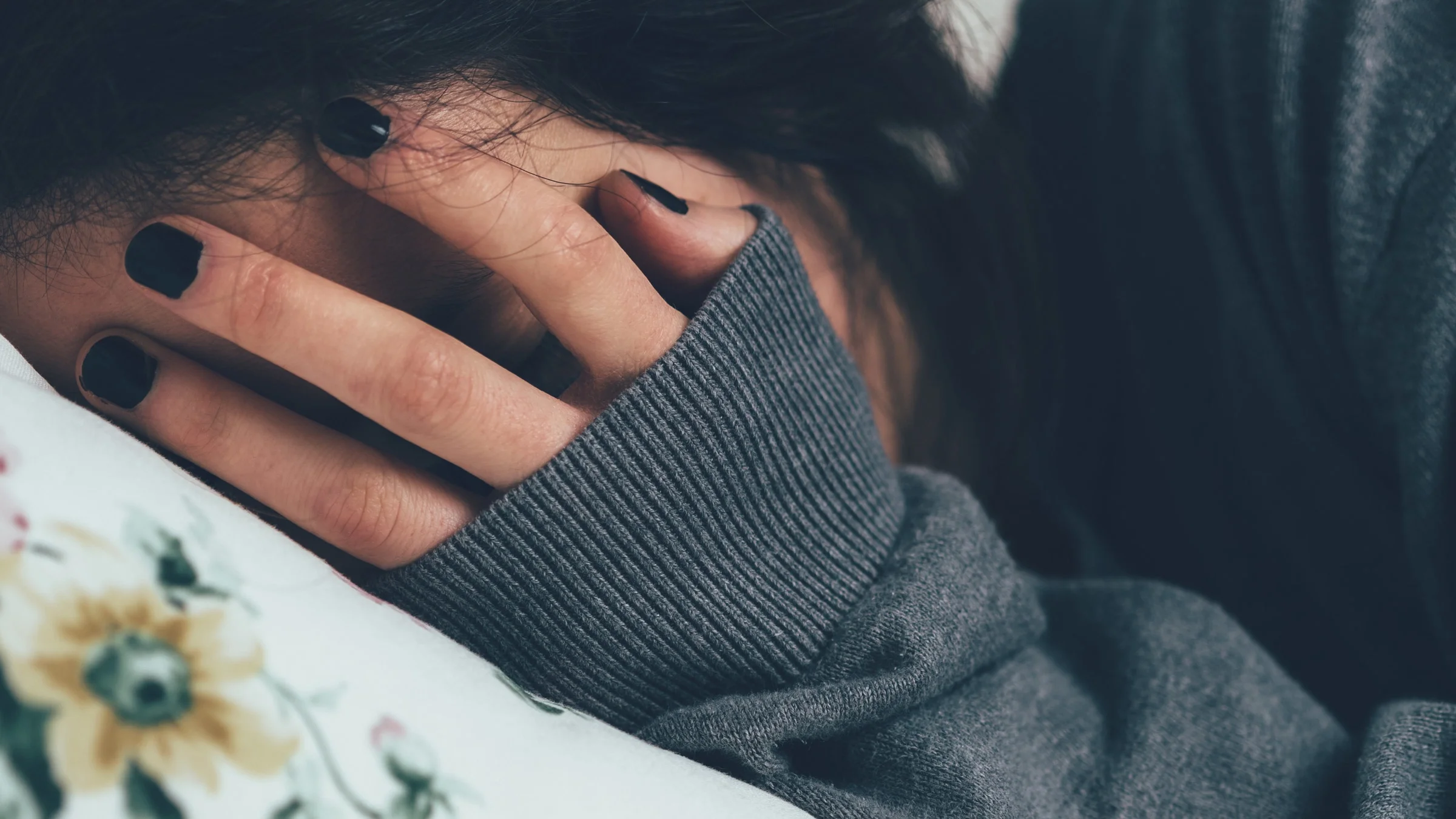 A person crying in bed with their palm on their face.