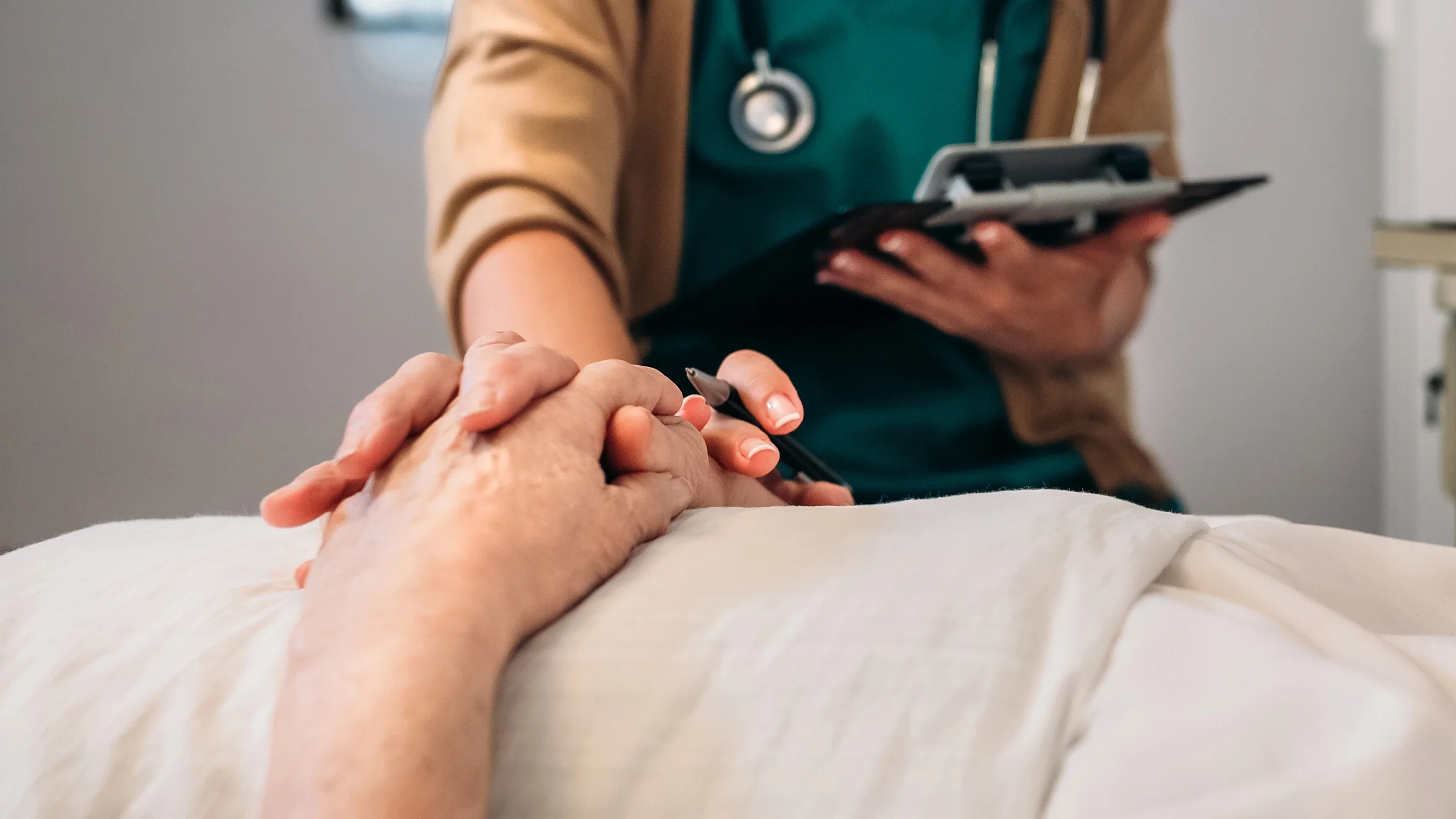 Close-up of a nurse holding a patient's hands on their chest.