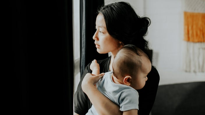 A person carrying their baby and looking outside their window.