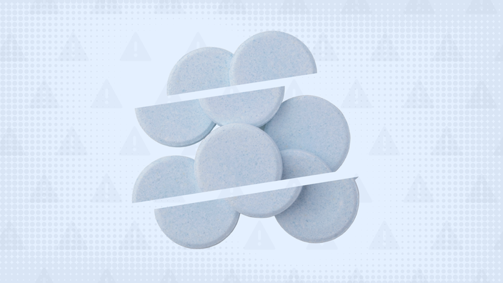 Light blue background with texture and warning sign pattern. In the center is a pile of round blue chalky-looking pills cut into thirds. 