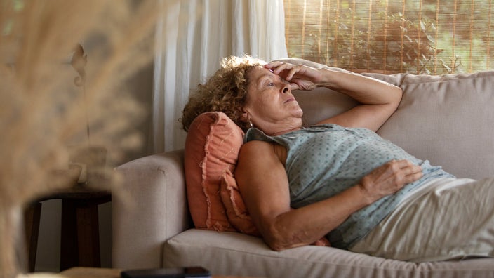 A woman feels dizzy and lies on a couch. Having low levels of potassium can lead to dizziness, lightheadedness, and even fainting. 