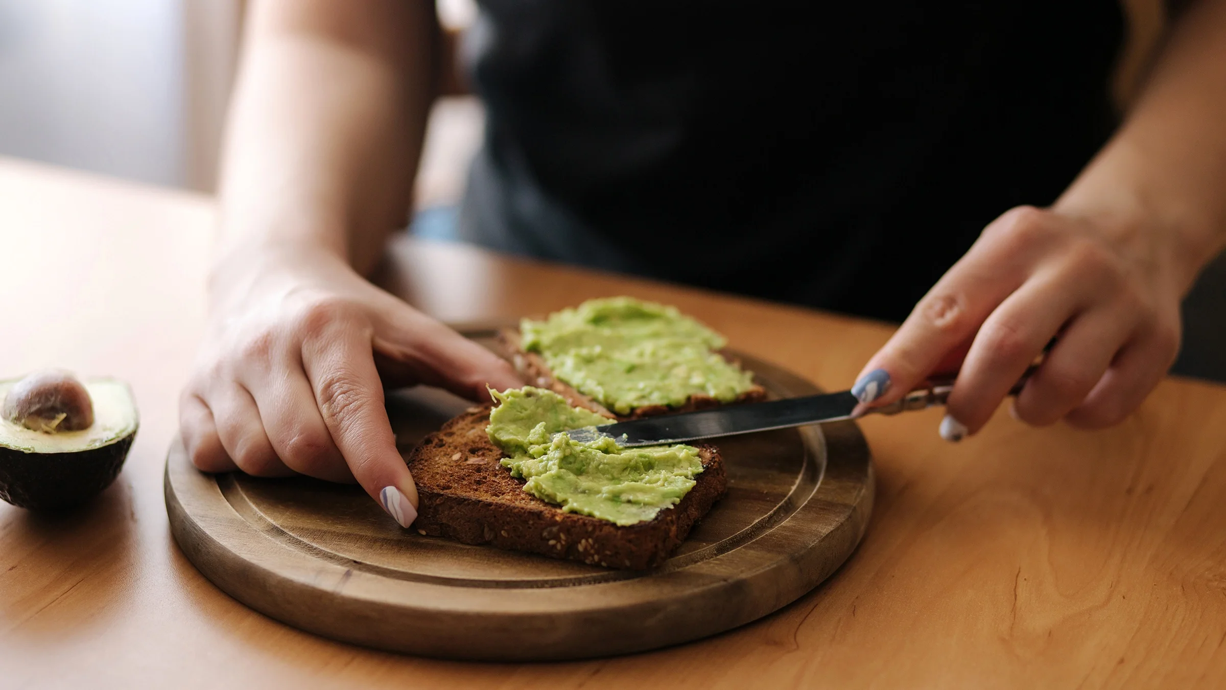 Close-up of someone spreading avocado on a piece of toast.