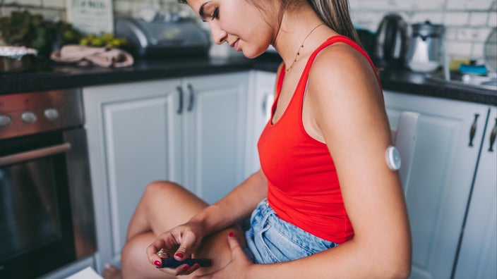 Young woman sitting with her legs crossed using an insulin injector on her thigh.