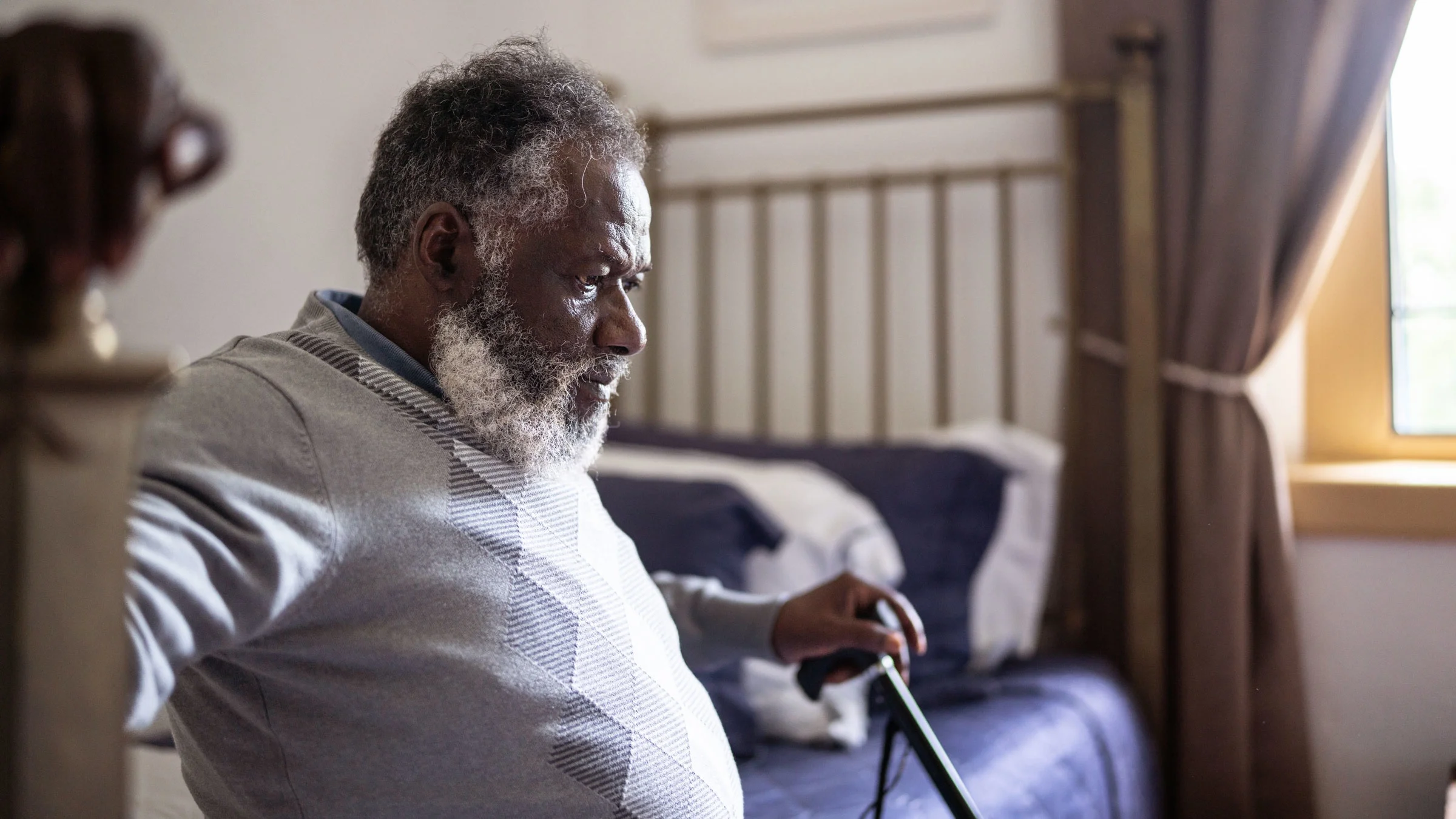 Contemplative older man sits on the edge of his bed at home.
