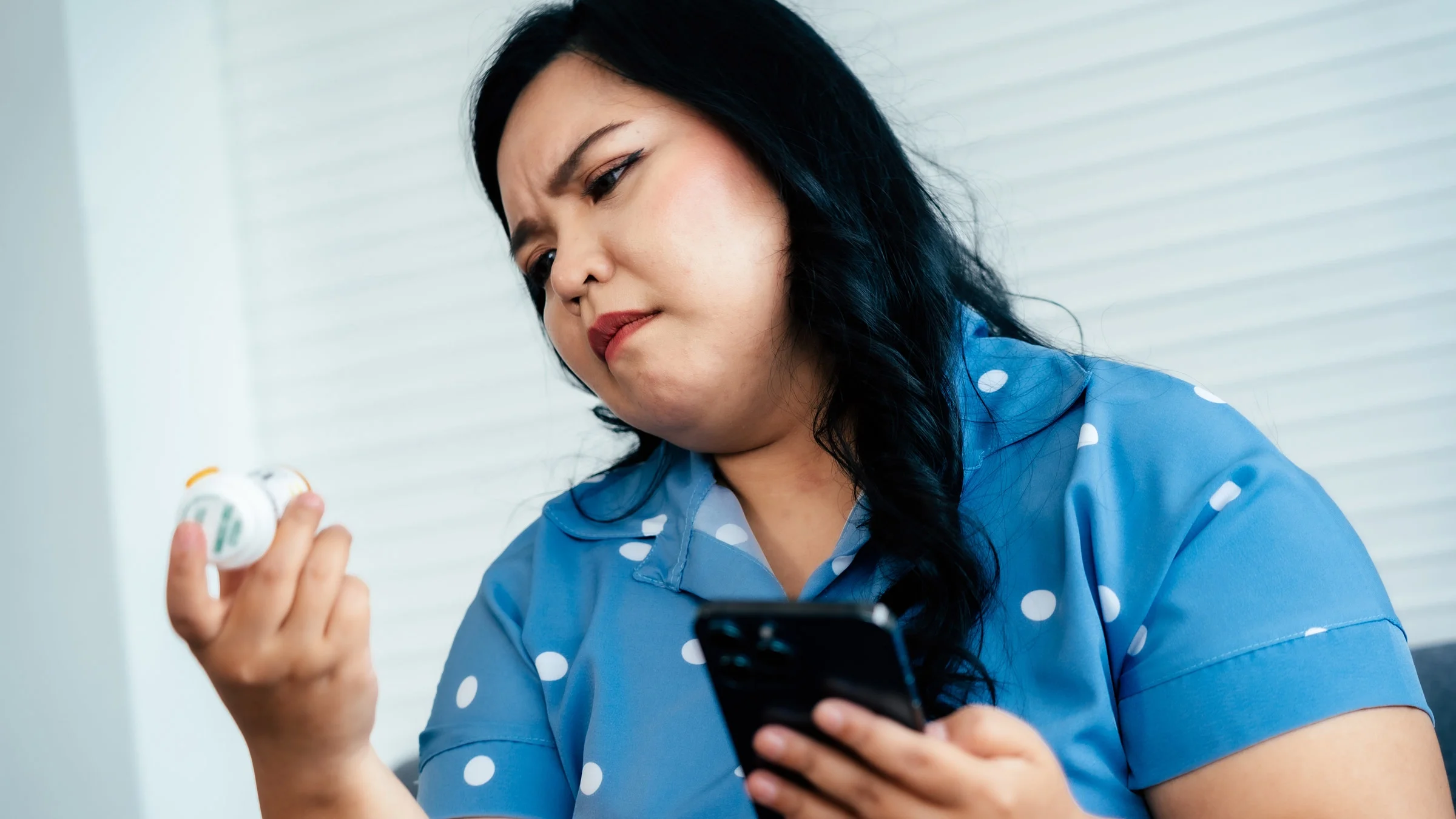 A plus-size person examining a pill bottle and looking it up on their phone.