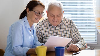 caregiver-elderly-man-reading-paper-926313098