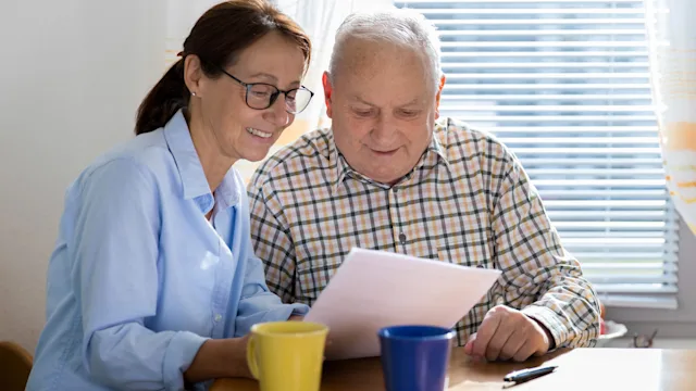 caregiver-elderly-man-reading-paper-926313098