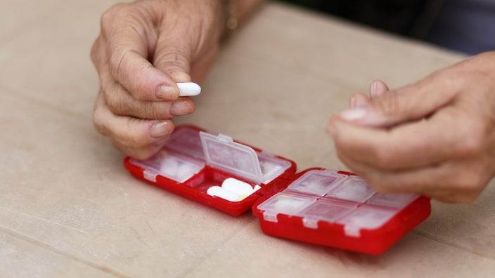 A close-up of hands taking pills from an organizer.