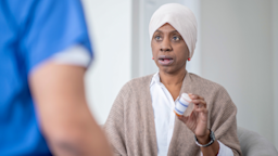 A cancer patient holding a pill bottle, talking to a HCP. 
FatCamera/E+ via Getty Images 
