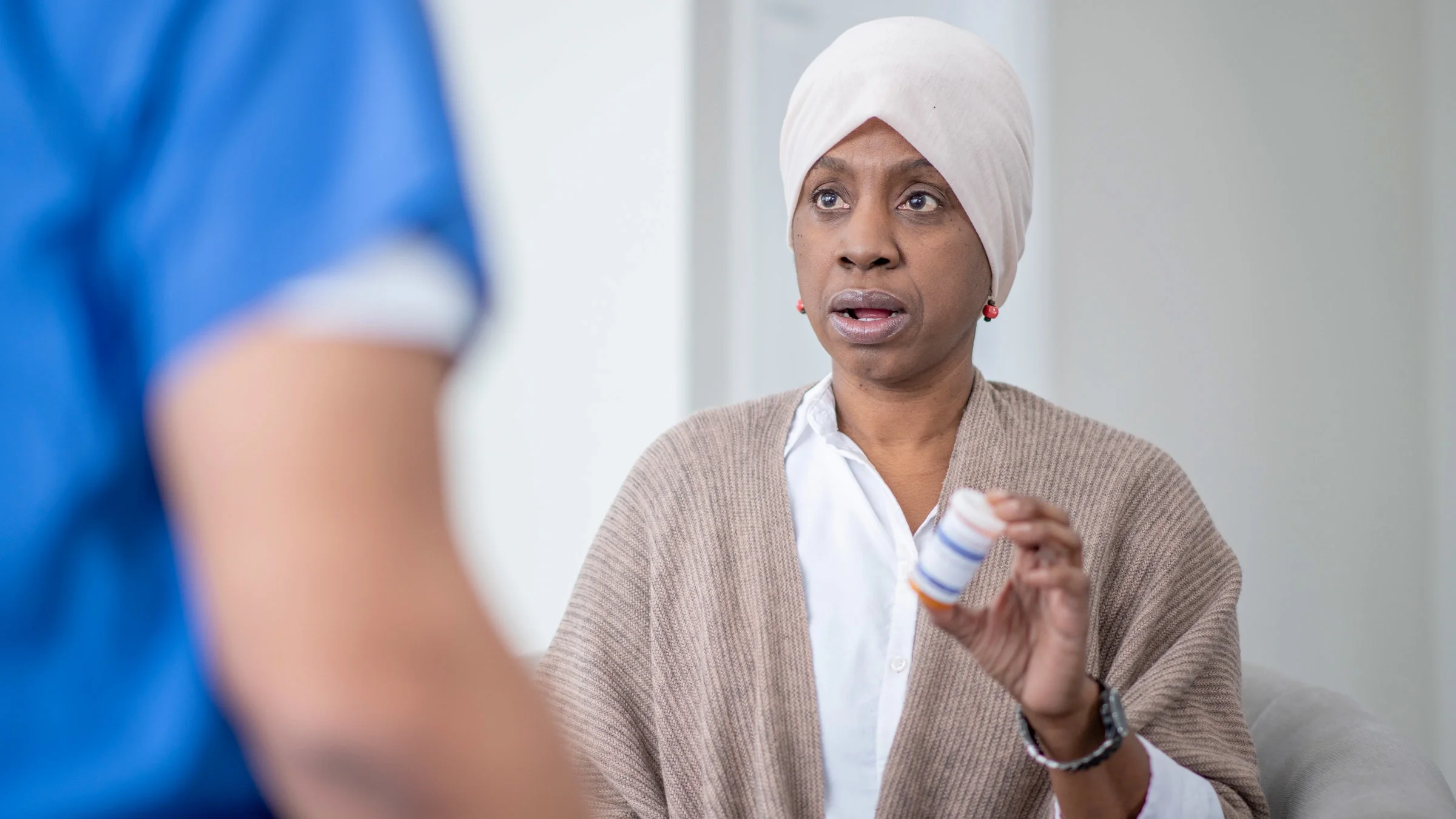 A cancer patient holding a pill bottle, talking to a HCP. 