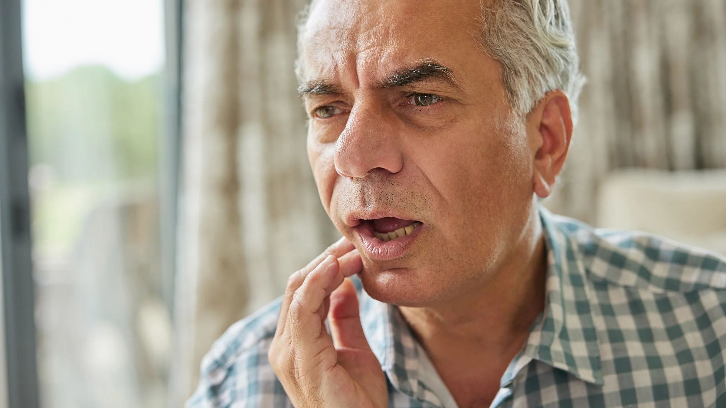 An older adult is rubbing the side of their jaw.