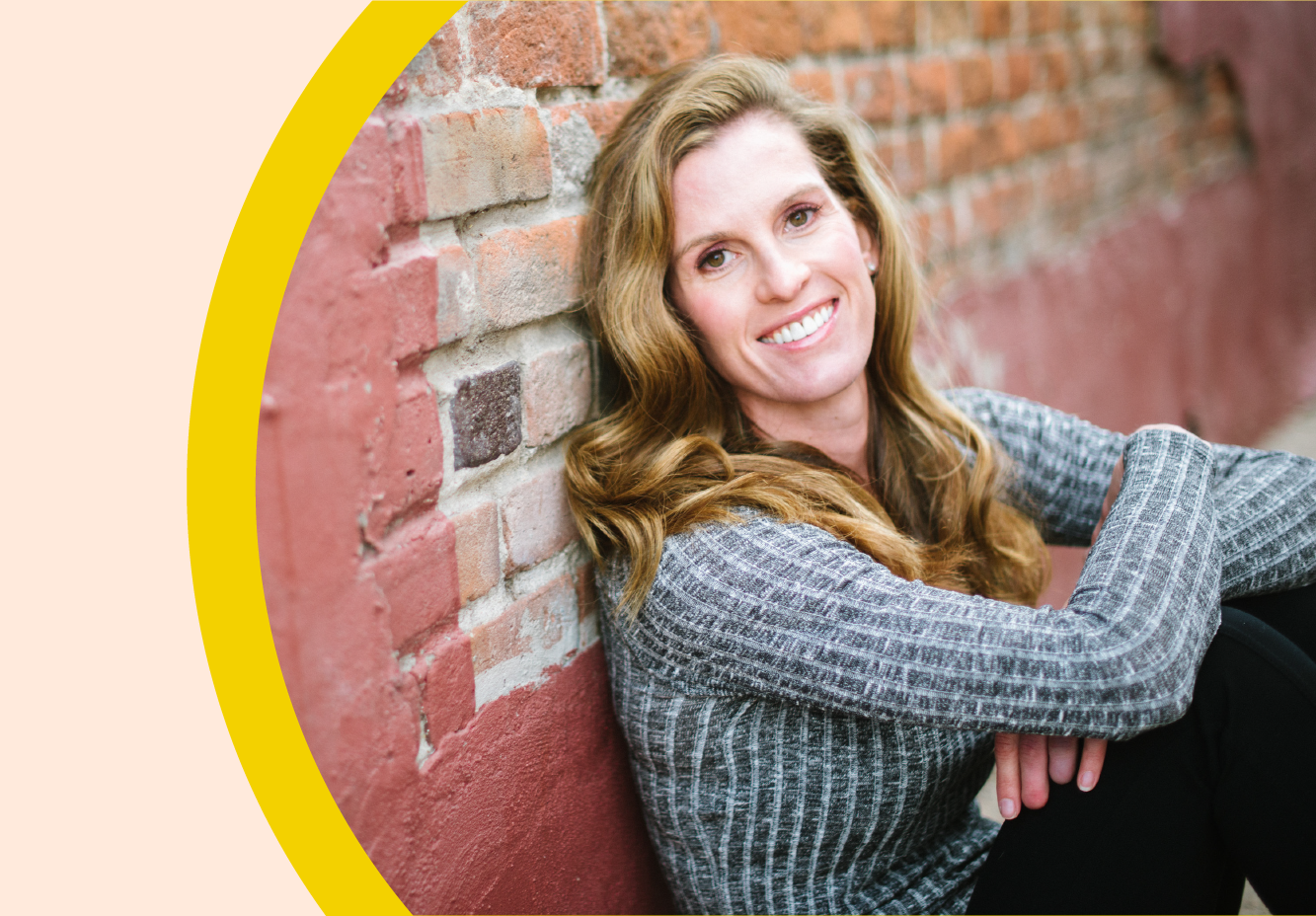 Portrait of Lindsay Weitzel leaning against a brick wall, outdoors.