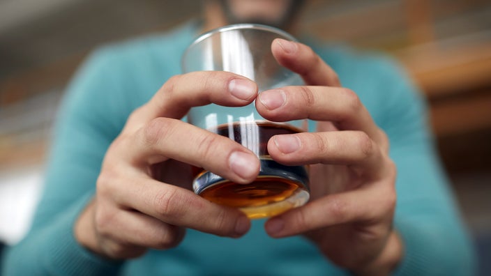 A man is holding a glass of bourbon in a close-up. 