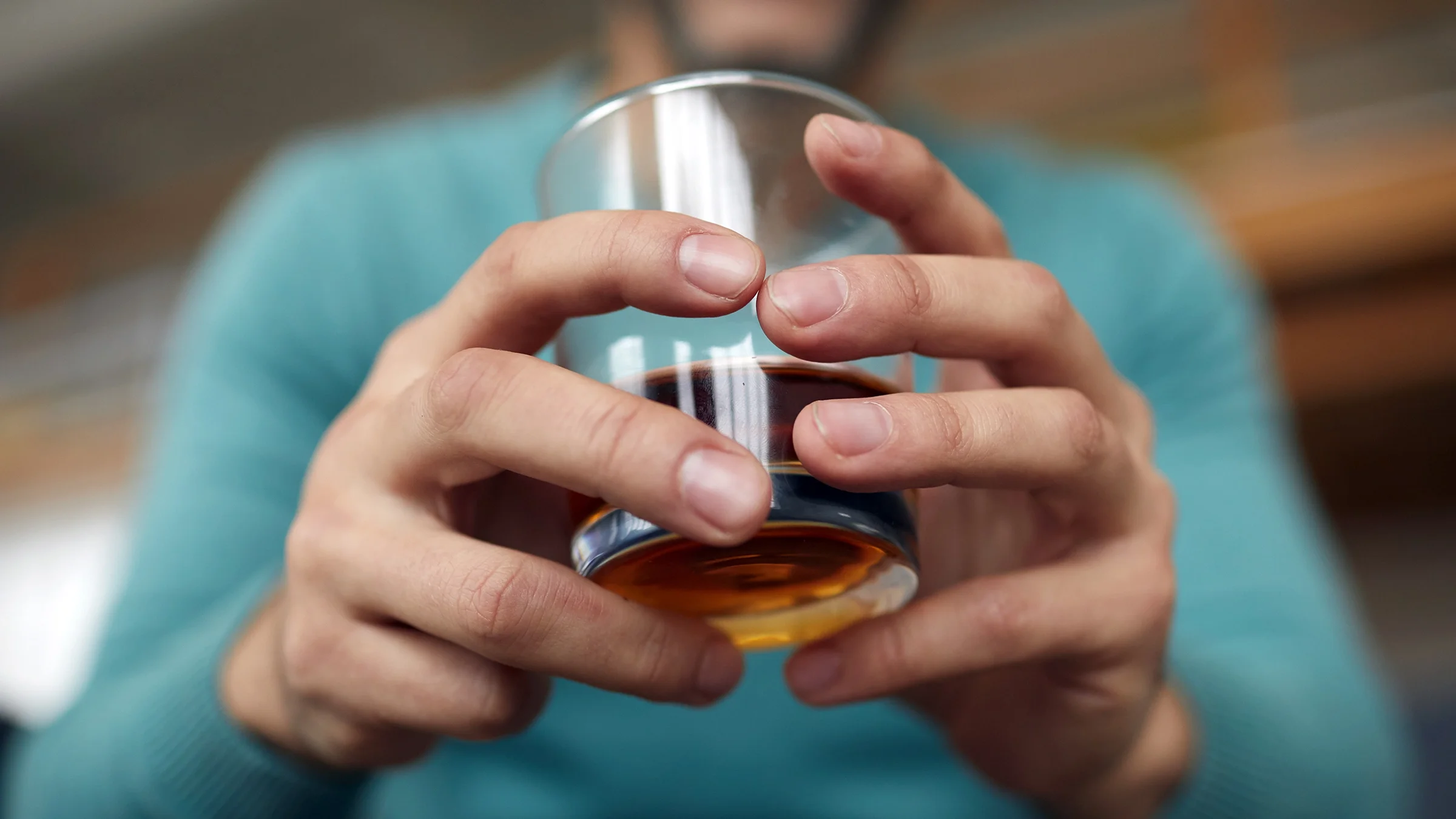 A man is holding a glass of bourbon in a close-up.
