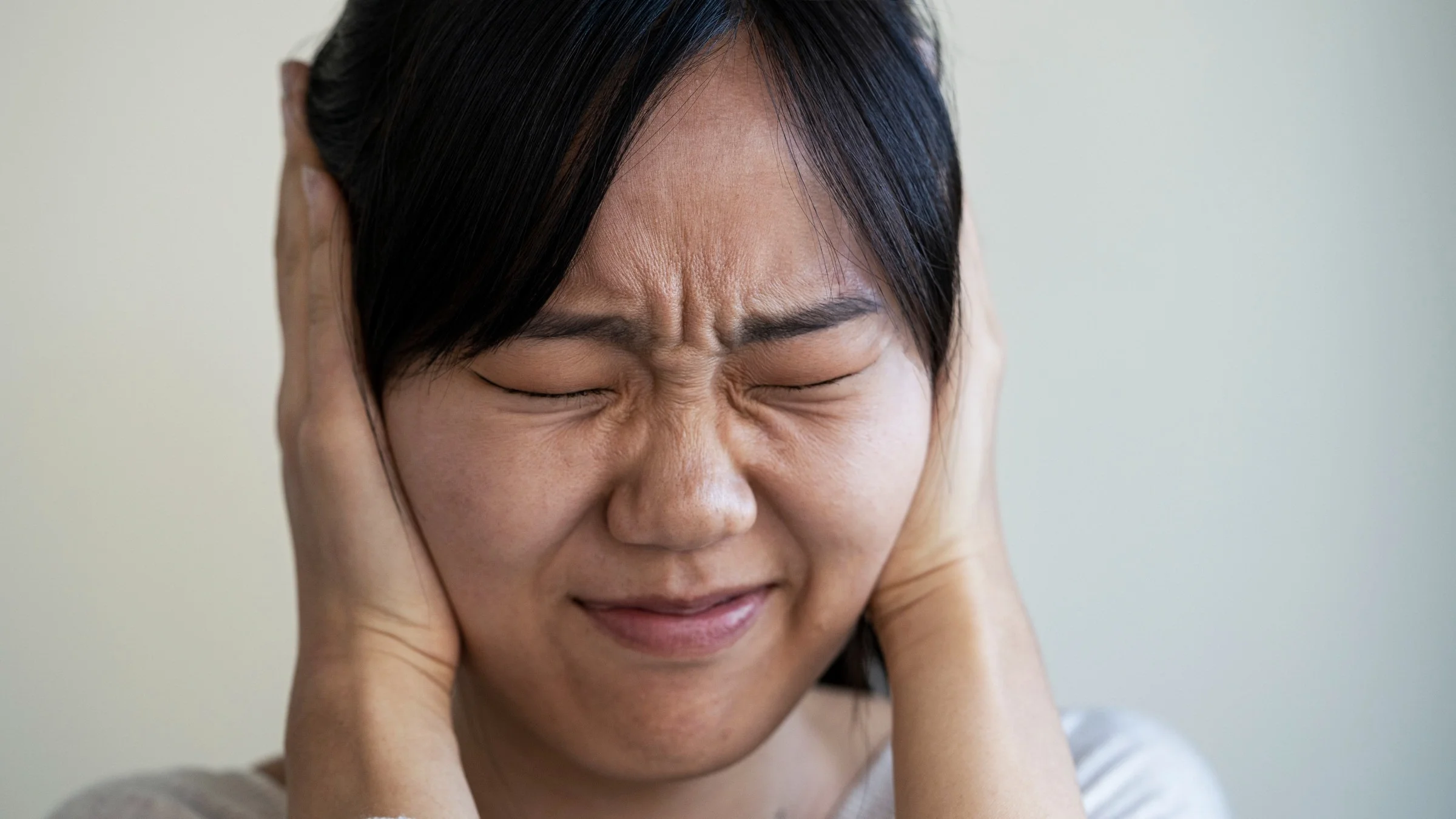 Close-up of a woman covering her ears and squinting.