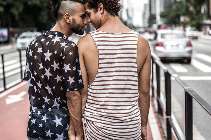 Queer couple walking down the street hand in hand leaning into each other while touching foreheads.
