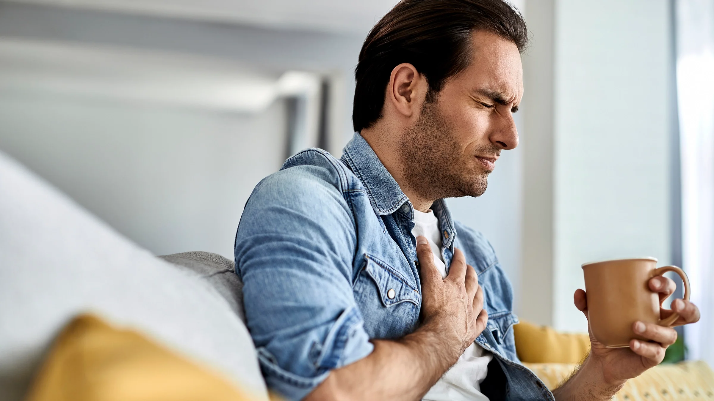 Man experiencing heartburn while drinking a cup of coffee.