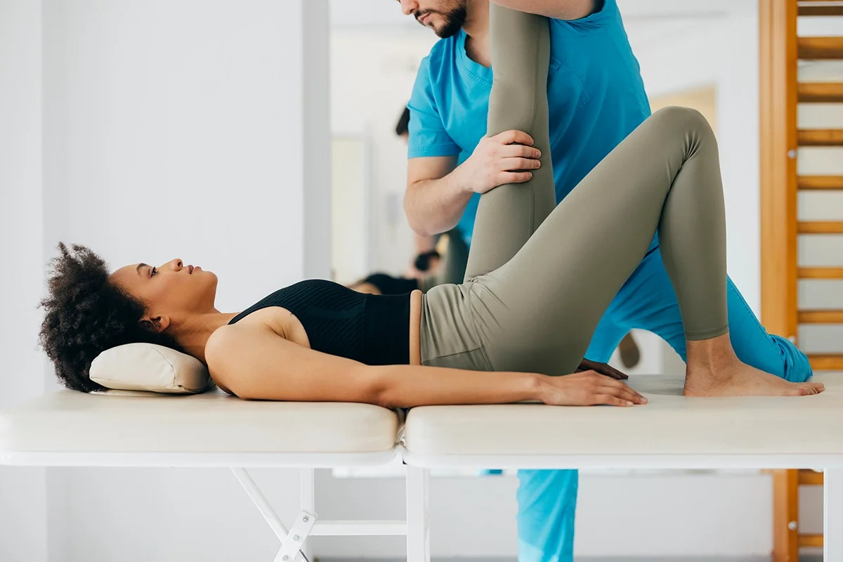 Young woman with back pain getting a chiropractic adjustment on the table. The doctor is working on her leg by helping stretch it at a 90 degree angle.