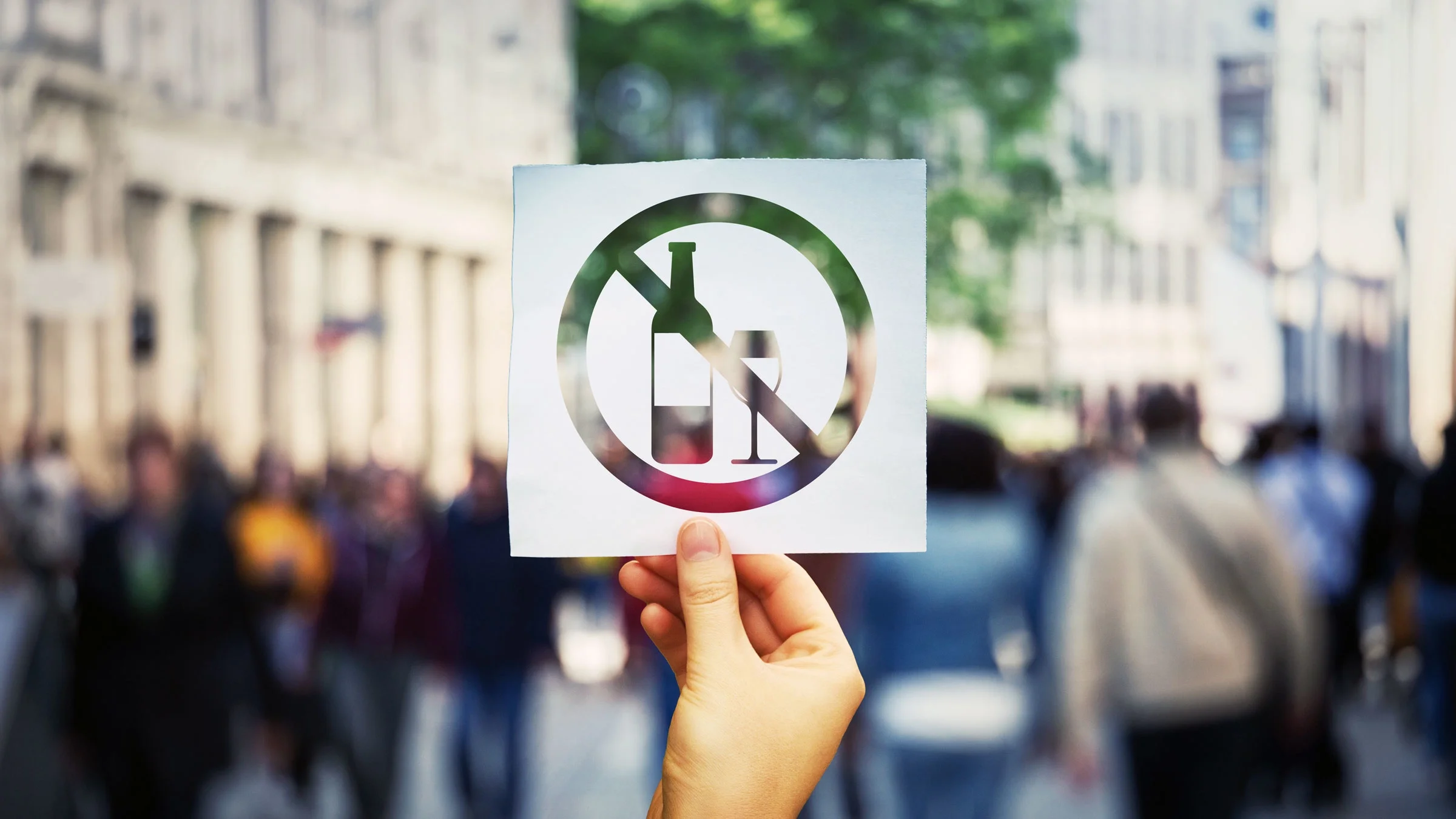 A person holds a “no alcohol” sign in their hand.