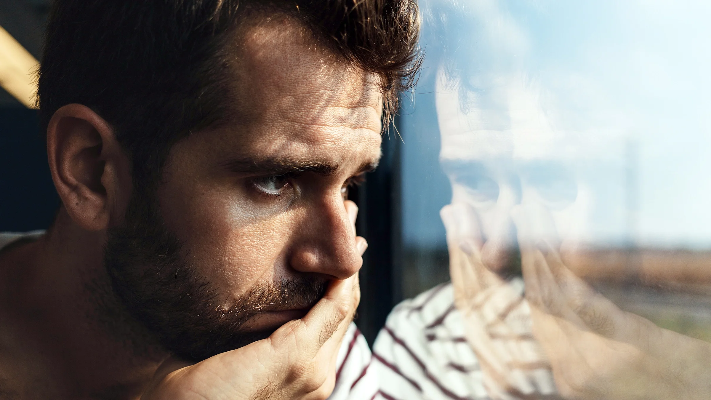 A man is looking out the window with a sad expression.