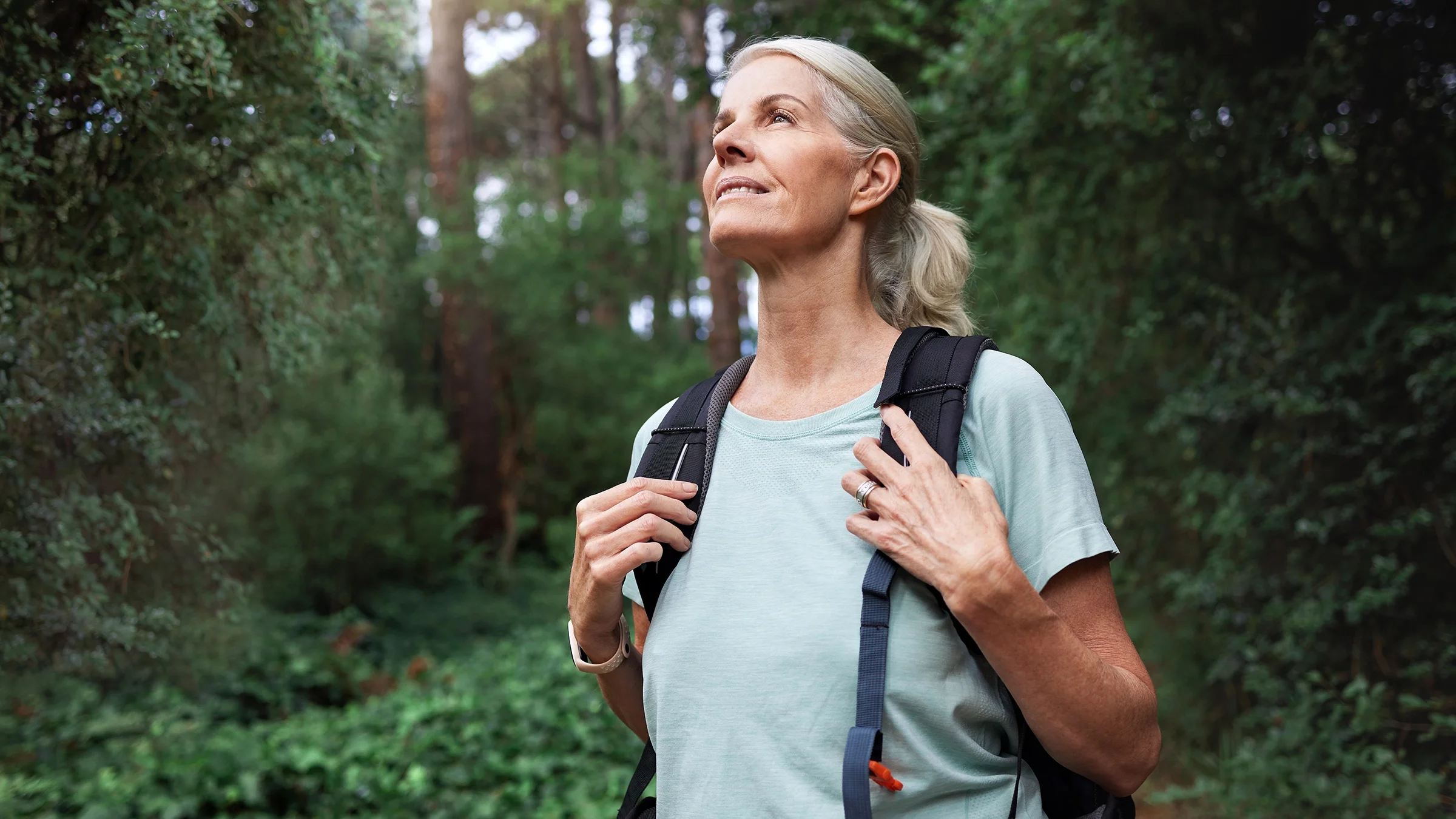 A woman wearing a backpack is walking in a wooded area.