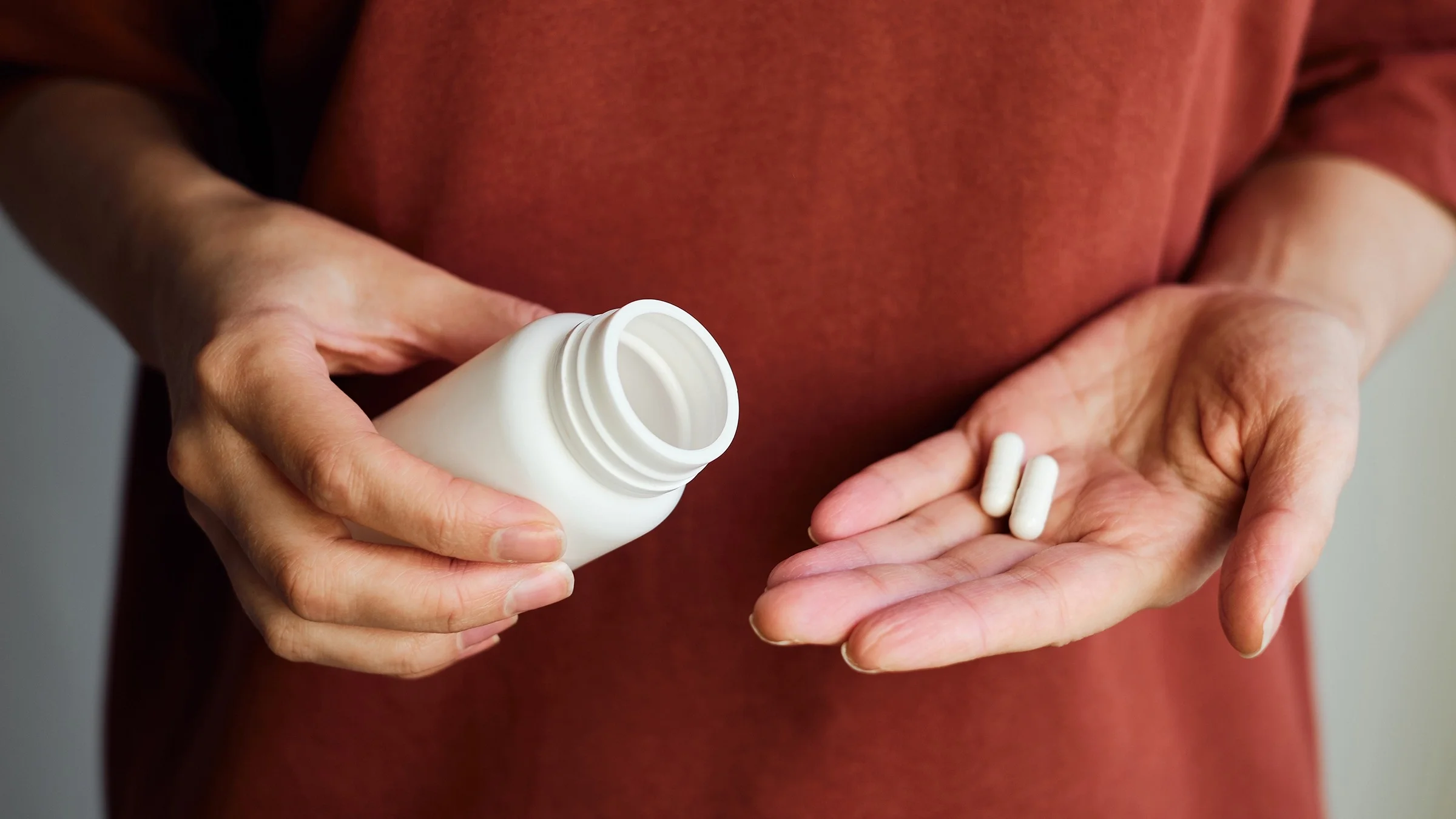 Close-up of woman pouring white pills into her hand wearing a dark red shirt