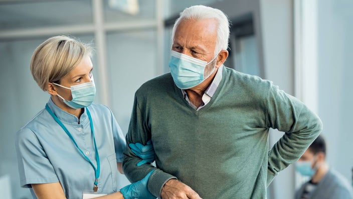 A patient with back pain, being helped by a HCP.