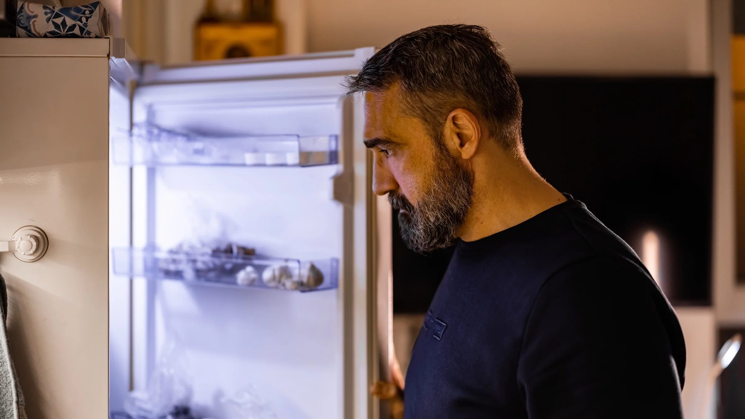 A man looks inside of his kitchen refrigerator.
