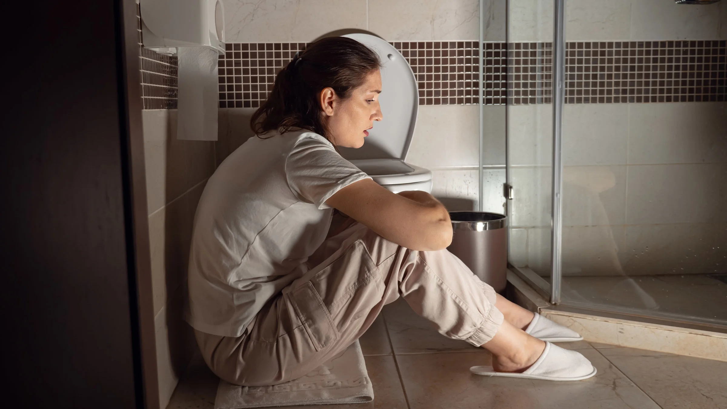 A nauseous person sitting crouched on a bathroom floor.