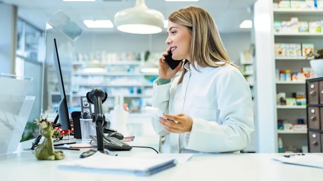 Pharmacists: Insurance: pharmacist on phone holding medicine 1482189403
