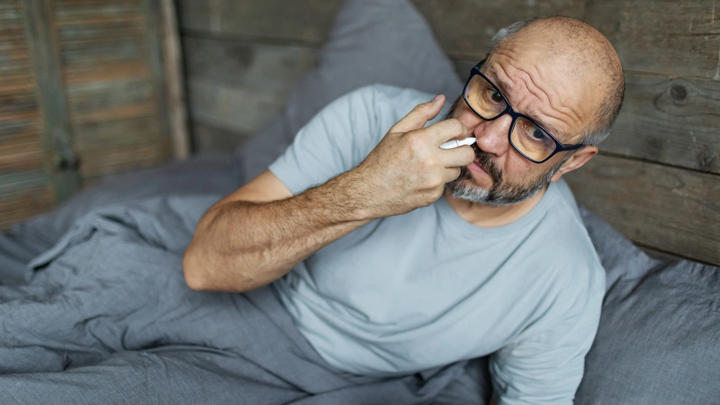 A man uses a nasal spray while in bed. 