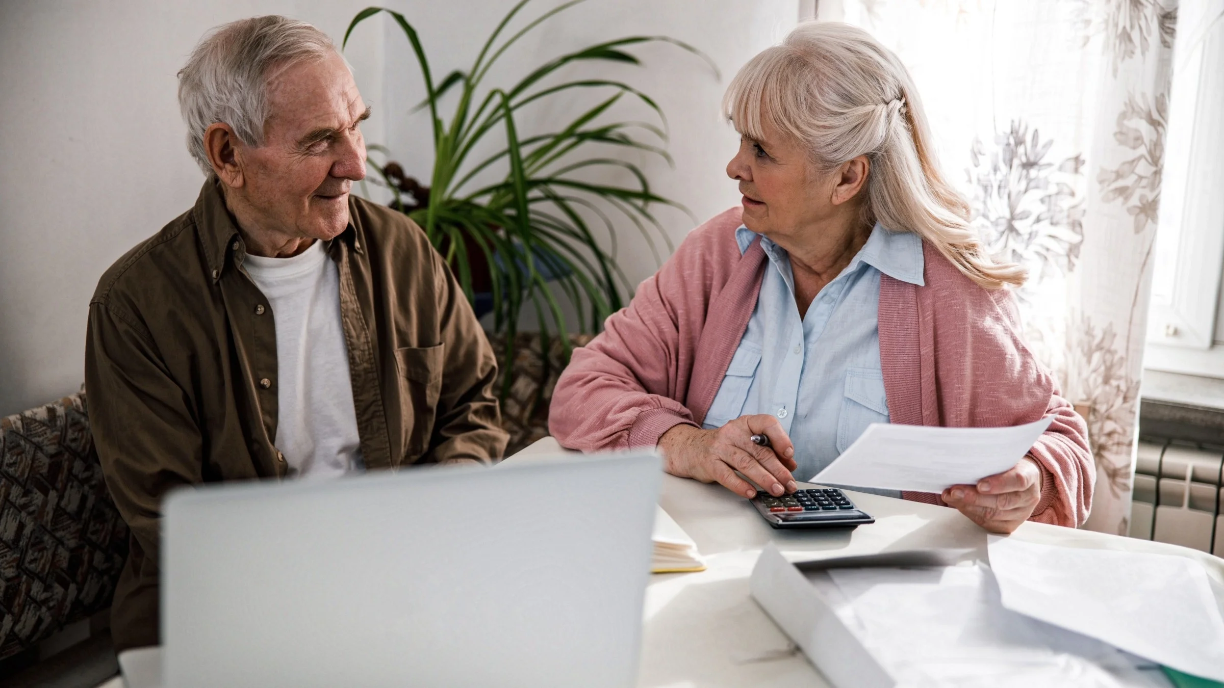 Senior couple sitting at the table reviewing documents and calculating cost at the dining table.