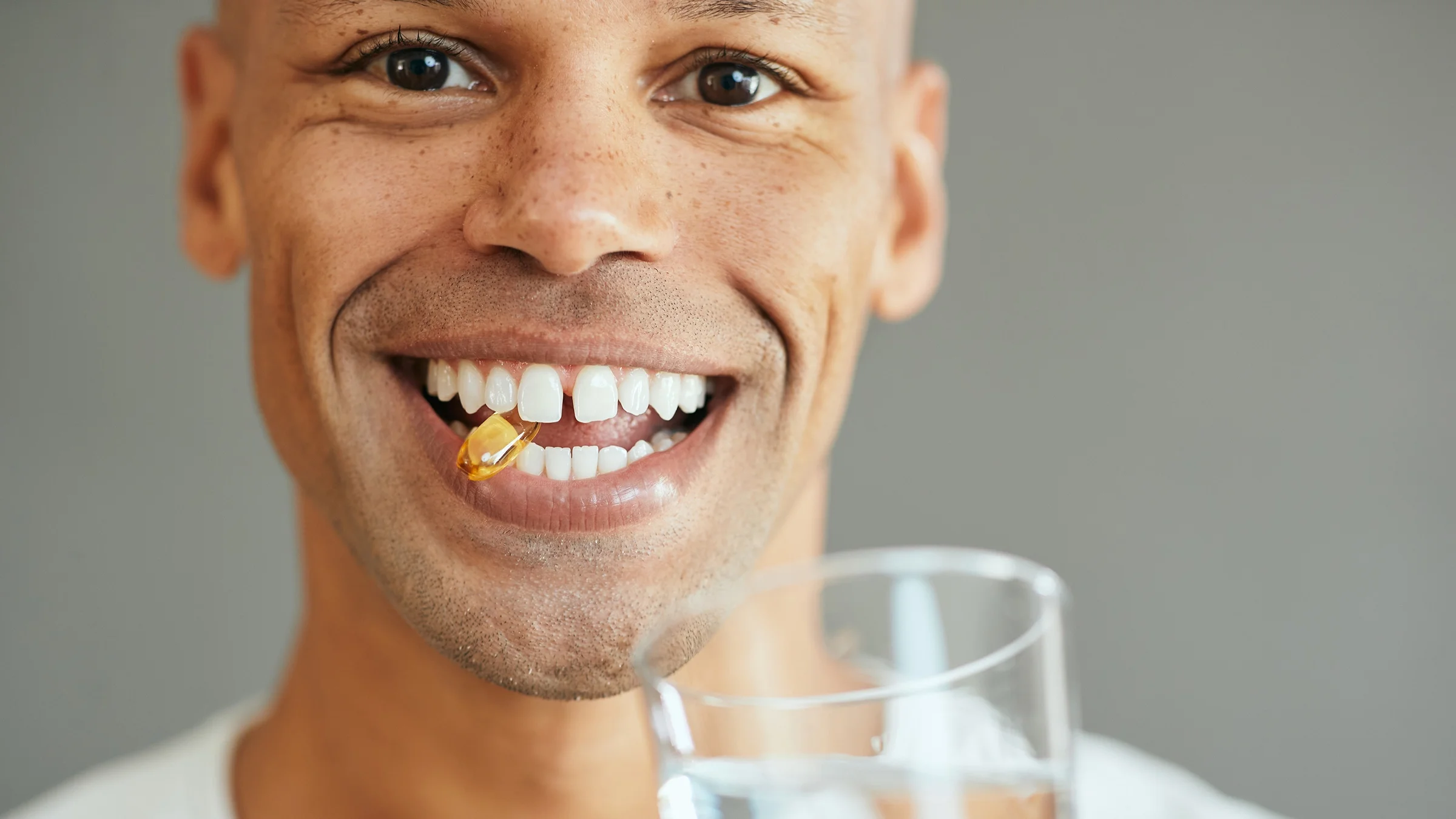Close-up of an extremely cute and extremely happy man smiling with a vitamin in his mouth.