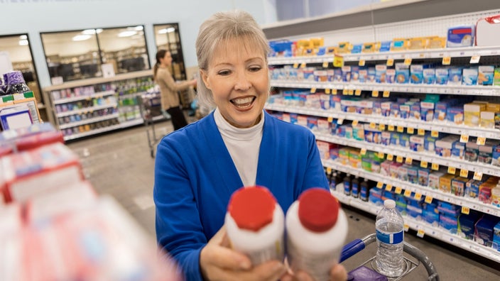 A customer holding two pill bottles in a pharmacy aisle.