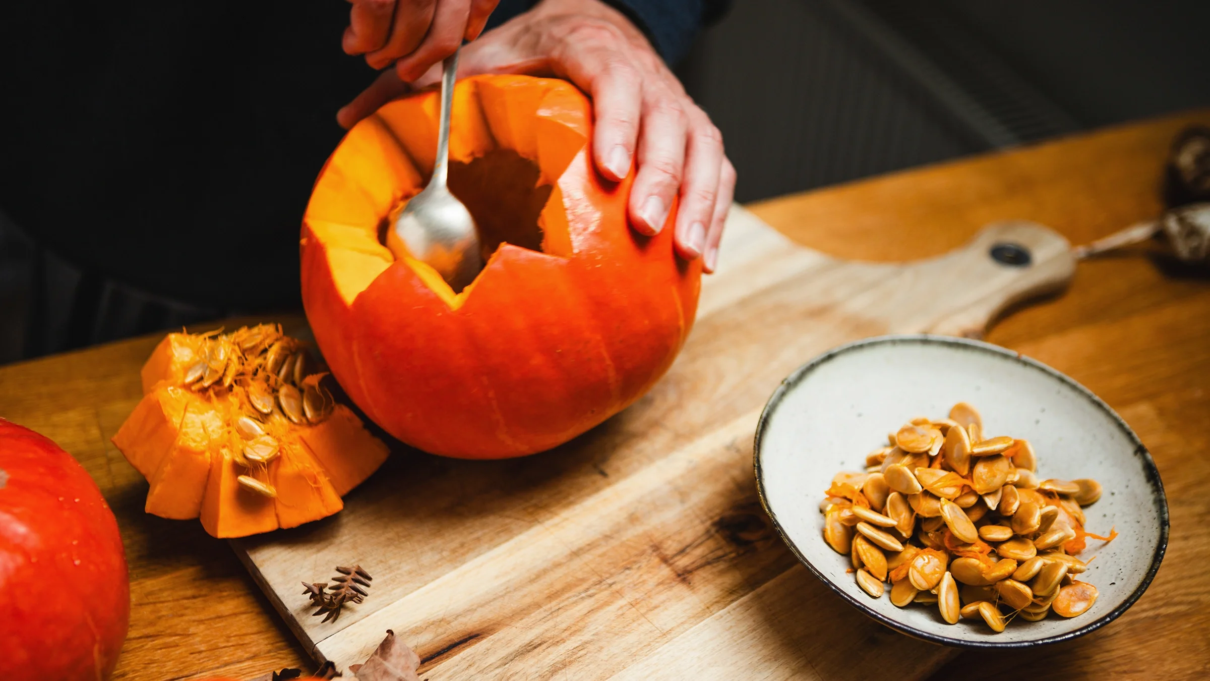 A man scoops up seeds out of a pumpkin.