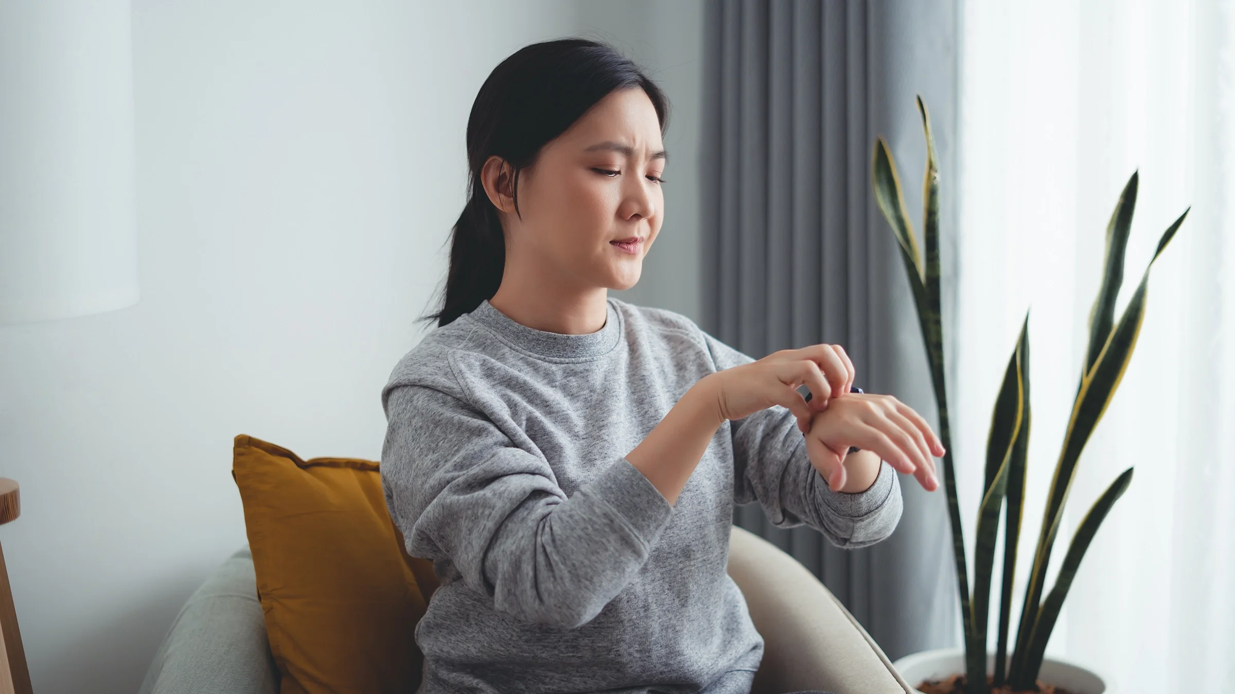 A woman suffering from irritated, dry skin scratches her hand while sitting at home.
