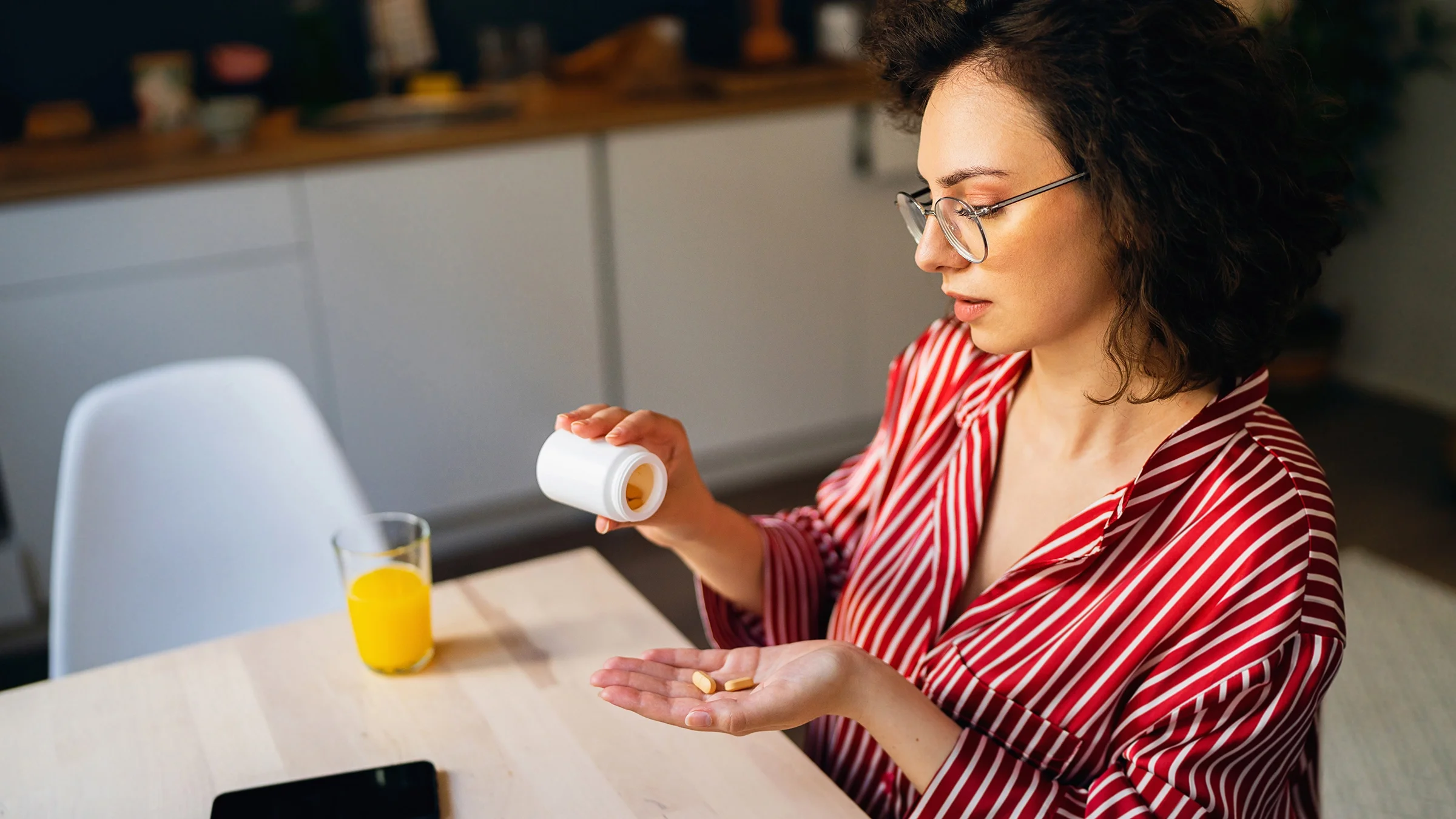 A woman takes medication while sitting at the kitchen table.