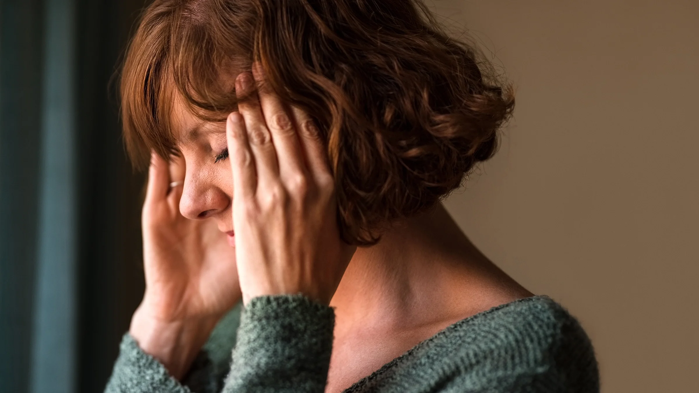 Close-up of a women with short hair looking worried with her hands at her temples.
