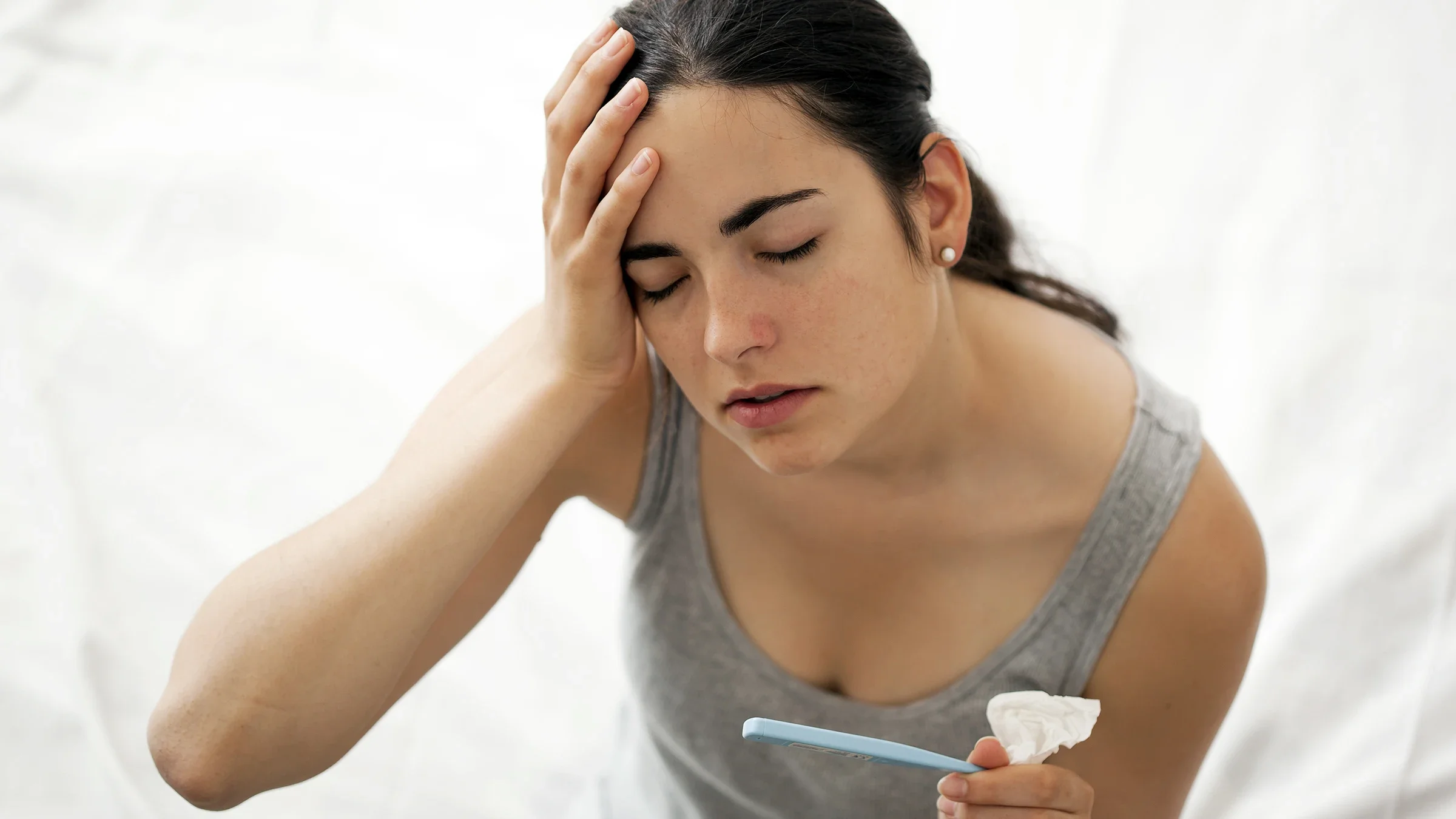 A woman feels her forehead as she checks her temperature on a thermometer.
Thomas_EyeDesign/E+ via Getty Images 